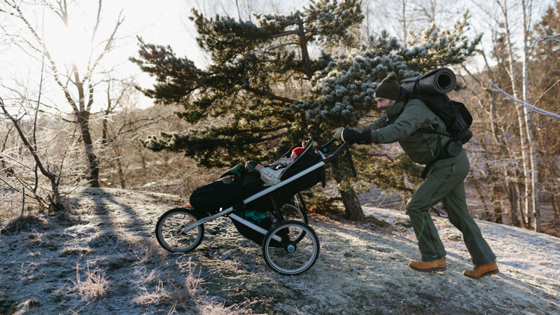 Mann i vinterlandskap skyver en barnevegn opp en bakke