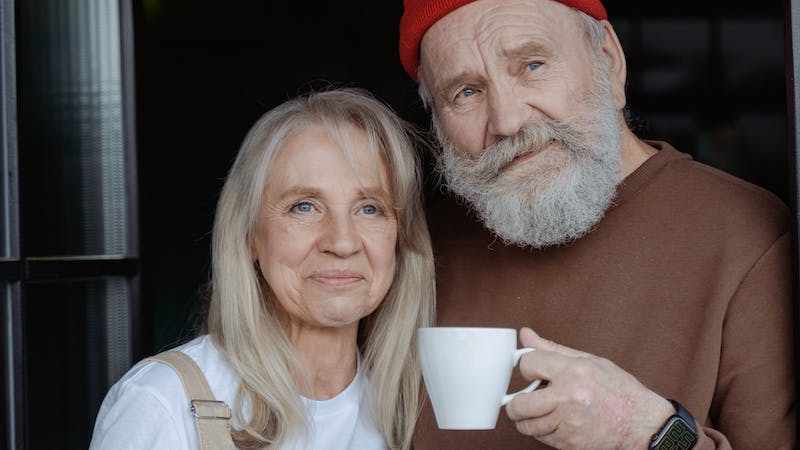 To eldre ser inn i kamera mens de drikker kaffe